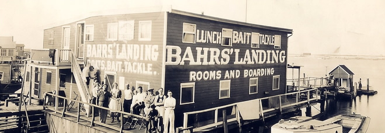 Black-and-white photograph of Bahrs Landing in its early days, crew gathered on the deck beneath painted Boats Bait Tackle signage