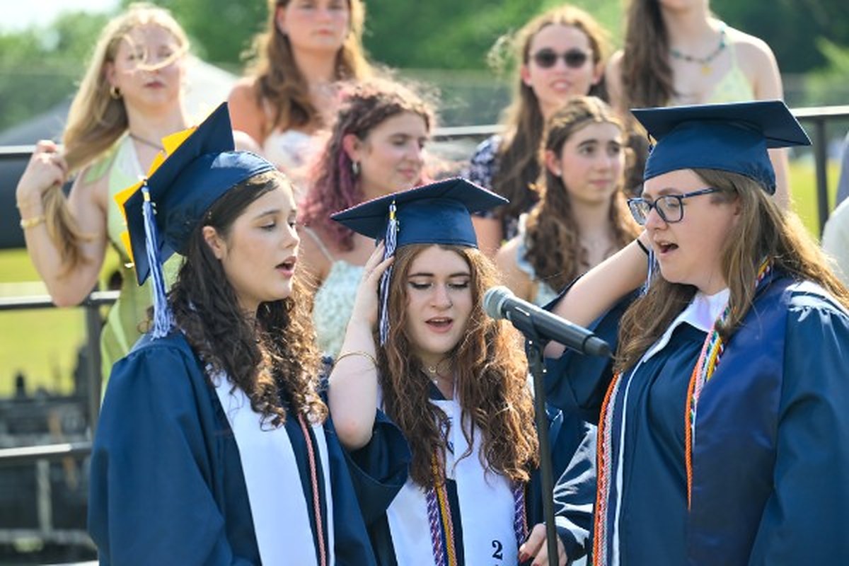 Ella singing with the choir at her high school graduation, at the microphone in cap and gown