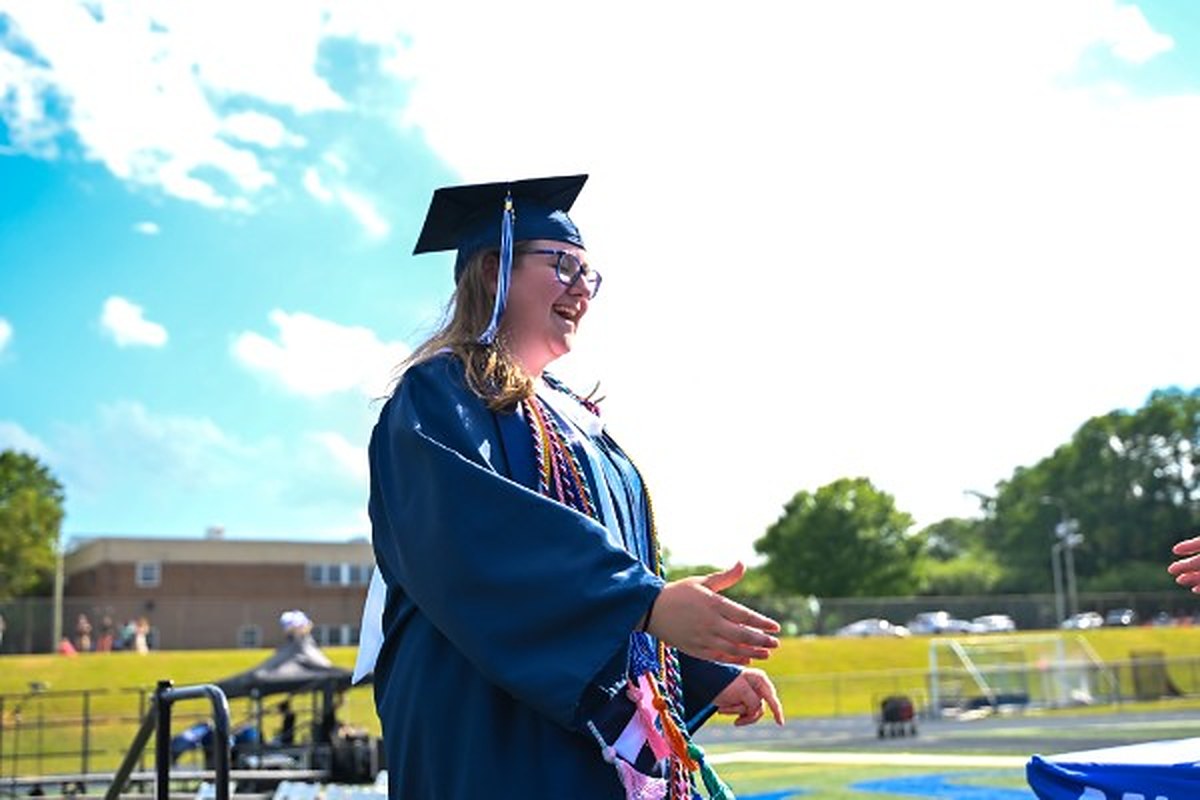 Ella beaming in cap and gown on graduation day, arms open
